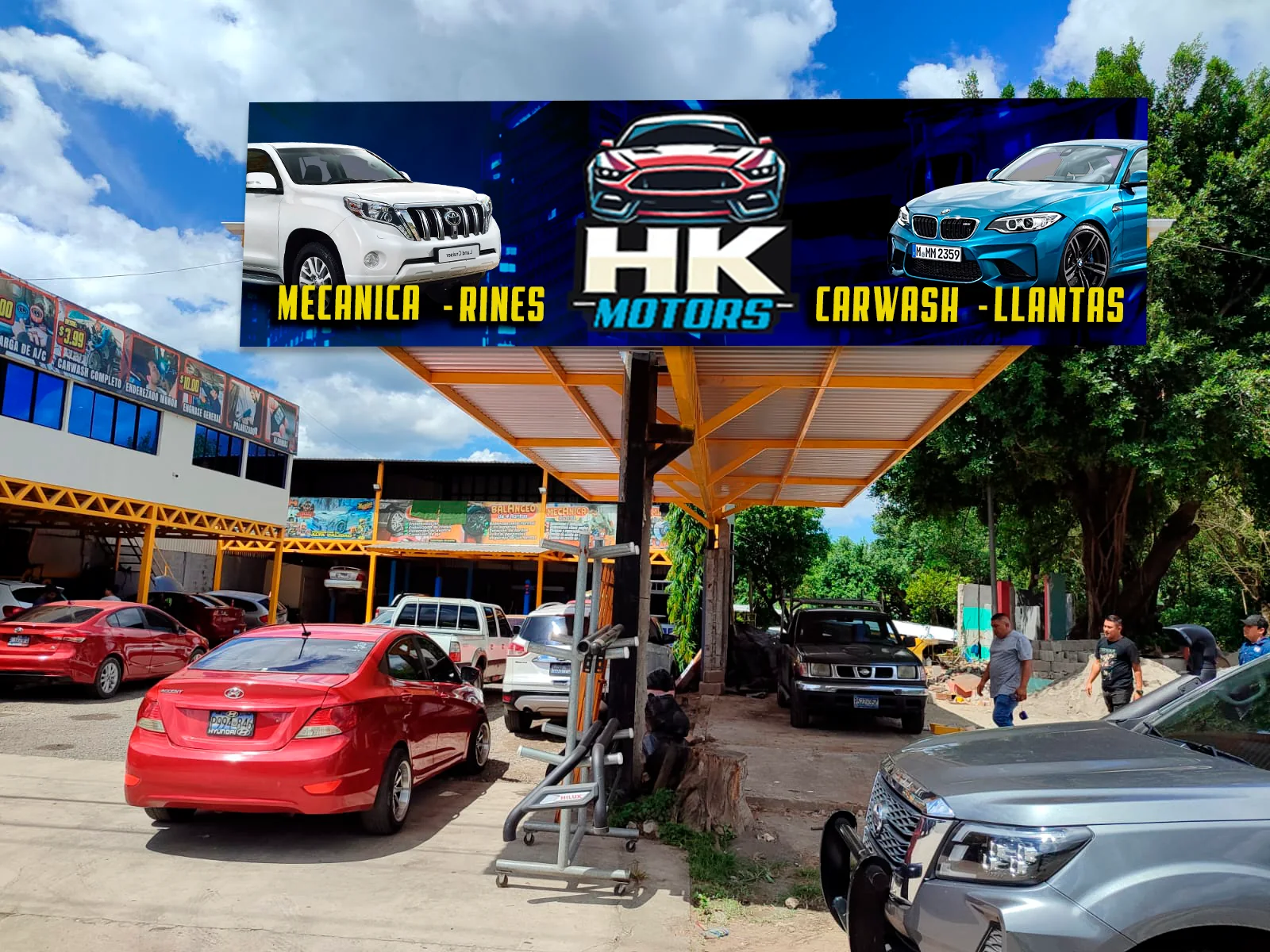 Rótulo de HK Motors sobre la isla frontal del taller con sus servicios de mecánica, rines, carwash y llantas